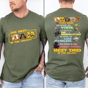 Puede incluir: Camiseta verde oliva con el texto "THE BEST DAD IN THE GALAXY" en amarillo y naranja en la parte delantera. La parte trasera de la camiseta tiene el texto "DADDY" y personajes de Star Wars.