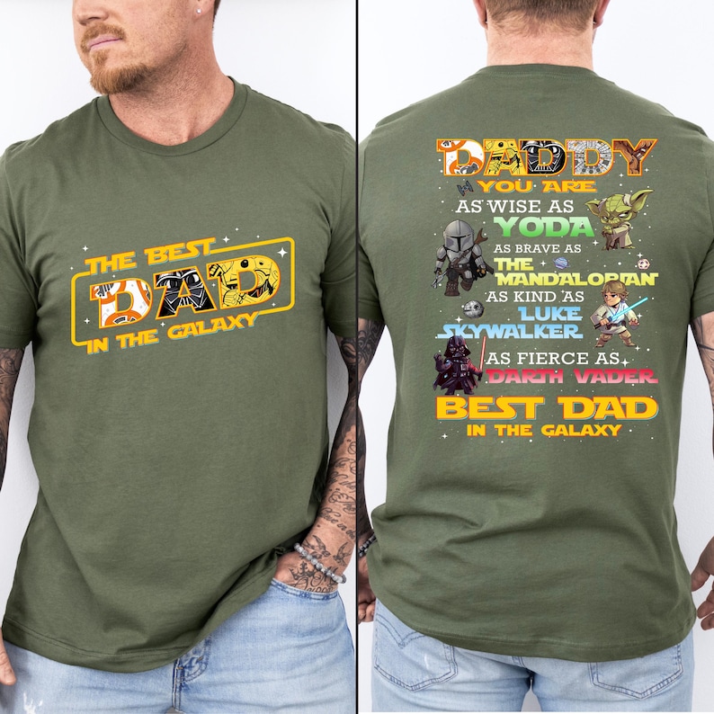 Puede incluir: Camiseta verde oliva con el texto "THE BEST DAD IN THE GALAXY" en amarillo y naranja en la parte delantera. La parte trasera de la camiseta tiene el texto "DADDY" y personajes de Star Wars.