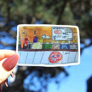 May include: A sticker depicting a hand-drawn pizza shop illustration. The shop features a counter with food, a menu board, and a pizza graphic. The sticker is held by a hand with maroon nail polish.
