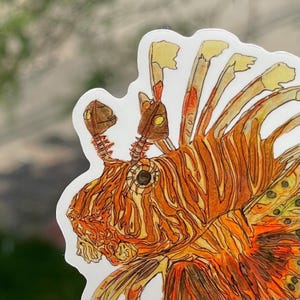 May include: A sticker featuring a detailed illustration of a lionfish. The artwork showcases the fish's orange and yellow striped body, with intricate details in the fins and head. The sticker has a white border and is likely for decorative purposes.