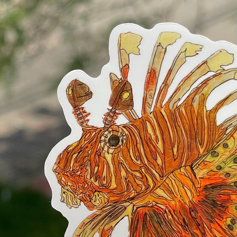 May include: A sticker featuring a detailed illustration of a lionfish. The artwork showcases the fish's orange and yellow striped body, with intricate details in the fins and head. The sticker has a white border and is likely for decorative purposes.