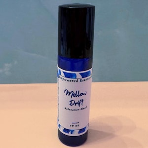 May include: A dark blue essential oil roller bottle with a black cap. The label reads "Mellow Drift Relaxation Blend" in script. The bottle contains 10 ml of product.