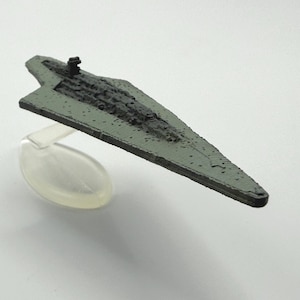 May include: A miniature model of a starship, featuring a gray and black color scheme. The ship has a triangular design with detailed surface textures and is mounted on a clear stand, suggesting a display piece or collectible item.
