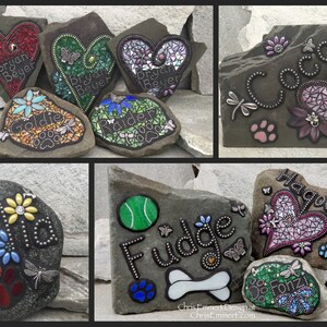 May include: A collection of decorative stone pet memorials. Each stone features a mosaic design, names, paw prints, and dragonfly or butterfly accents. The stones are in various shapes and colors, suitable for garden or home decor.