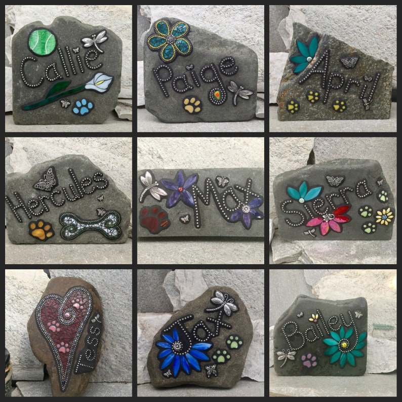 May include: Nine decorative stone plaques with names, flowers, paw prints, and dragonflies. The names include Callie, Paige, April, Hercules, Max, Sierra, Tessy, Jax, and Bailey. Each stone has a unique design with colorful accents.