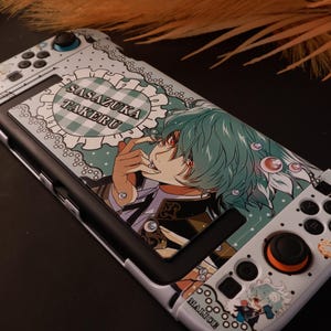 Könnte beinhalten: Eine weiße Spielkonsolen-Hülle mit einem Anime-Charakter mit türkisem Haar und roten Augen. Das Design zeigt einen herzförmigen Rahmen mit dem Text SASAZUKA TAKERU, ein kleines MALICE-Etikett und verschiedene kreisförmige Akzente auf Punkten.