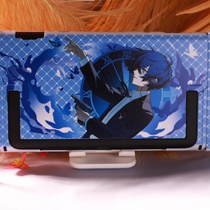 May include: A blue protective console case featuring an anime-style character with dark hair and headphones, wearing a suit and holding a handgun. The background displays a large clock face, butterfly silhouettes, and a white diamond grid pattern.