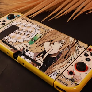 Puede incluir: Una funda amarilla para consola de juegos con una ilustración estilo anime de un personaje de cabello rubio y ojos verdes. El diseño incluye un borde festoneado, un gráfico de tubo de ensayo verde y el texto RAISHI GEYUKI y MALICE impreso.