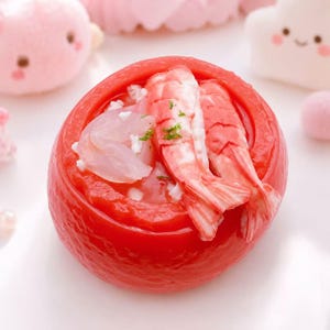 May include: A vibrant red, tomato-shaped dish filled with shrimp and other ingredients. The shrimp are pink and white, with a few green herbs sprinkled on top. The dish is set against a soft, light background.