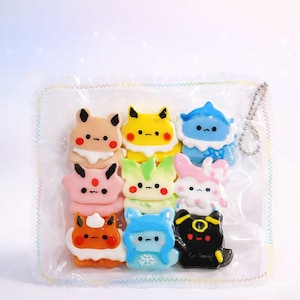 May include: A selection of colourful, cartoon-style character macarons in a clear plastic bag. The macarons feature various designs with different colours, including yellow, blue, pink, and orange. Each macaron has a unique face and design.