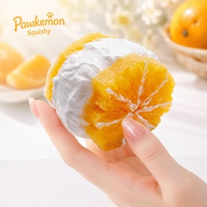 May include: A Pawkemon Squishy toy shaped like an orange slice sandwich with a thick layer of white cream filling between two bright orange citrus segments. The texture appears soft and pliable, featuring realistic orange pulp details and white pith.