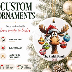 K&ouml;nnte beinhalten: Ein rundes, wei&szlig;es Keramikornament mit einem Cartoon-Elch, der eine Weihnachtsm&uuml;tze tr&auml;gt. Der Elch h&auml;lt f&uuml;nf bunte Weihnachtskugeln mit den Aufschriften Mom, Dad, Noah, Charlie und Lucky. Unten steht der Text The Smith Family und 2026.