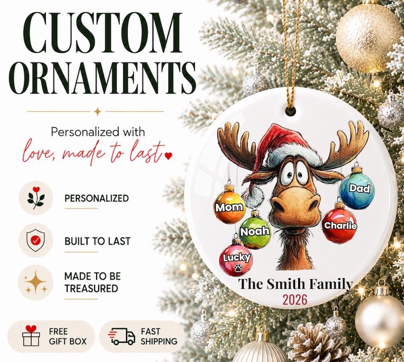 K&ouml;nnte beinhalten: Ein rundes, wei&szlig;es Keramikornament mit einem Cartoon-Elch, der eine Weihnachtsm&uuml;tze tr&auml;gt. Der Elch h&auml;lt f&uuml;nf bunte Weihnachtskugeln mit den Aufschriften Mom, Dad, Noah, Charlie und Lucky. Unten steht der Text The Smith Family und 2026.