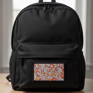 Op de afbeelding: Zwarte rugzak met een rechthoekige patch met een vlammenontwerp in rood, geel en oranje. De rugzak heeft een hoofdvak, een voorvak en twee zijvakken. Hij staat op een houten oppervlak.