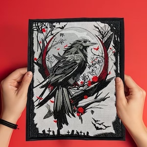 Op de afbeelding: Een rechthoekige geborduurde patch met een zwarte raaf op een tak voor een grote rode maansikkel. Het ontwerp bevat silhouetten van kale bomen, een spinnenweb, kleine rode rozen en grafstenen langs de onderste rand van de afbeelding.