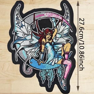 Op de afbeelding: Geborduurde patch met een fantasiefee met rood haar, een blauwe jurk en vleugels, zittend op een halve maan. De patch is 27,6 cm hoog en heeft een zwarte rand met decoratieve uitsparingen. De fee houdt een roze zeis vast.