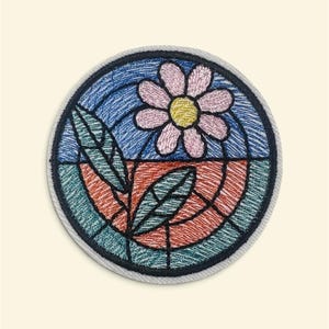Könnte beinhalten: Ein runder bestickter Aufnäher mit einem Design im Buntglasstil. Das Bild zeigt eine hellrosa Blume mit gelber Mitte, grünen Blättern und einem Hintergrund, der in blaue und orangefarbene Abschnitte unterteilt ist, alles mit schwarzem Garn umrandet.