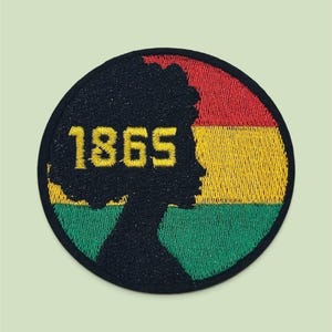 May include: A circular embroidered patch featuring a black silhouette of a person with an afro hairstyle. The background of the patch consists of horizontal red, yellow, and green stripes. The yellow numbers 1865 are stitched over the silhouette.