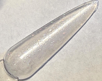 May include: A clear nail polish swatch with iridescent glitter. The swatch is shaped like a long, pointed oval and is attached to a clear plastic stick. The background is a light gray surface.