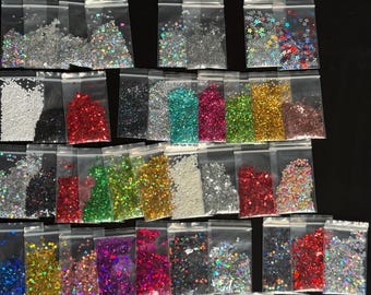 May include: A collection of small, clear plastic bags filled with various colors and shapes of glitter. The glitter includes silver, gold, red, green, and iridescent options, with shapes like stars, hearts, and confetti.