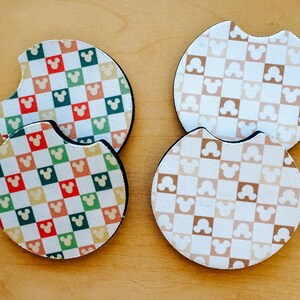 May include: Four round car coasters with a checkered pattern featuring Mickey Mouse silhouettes. Two coasters have a colorful pattern with red, green, yellow, and orange squares. The other two have a brown and white pattern.