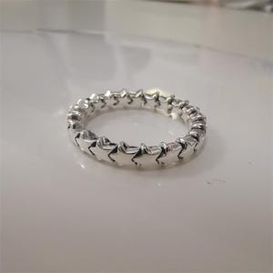 May include: A silver ring featuring a continuous pattern of star-shaped designs. The ring is made of a shiny, metallic material and is set against a white background. The stars are evenly spaced around the band.