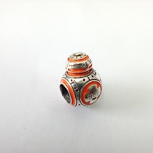 May include: A silver and orange charm with a spherical design. The charm features a detailed design with orange enamel accents and the word "PANDORA" engraved on the top. The charm is a collectible item.
