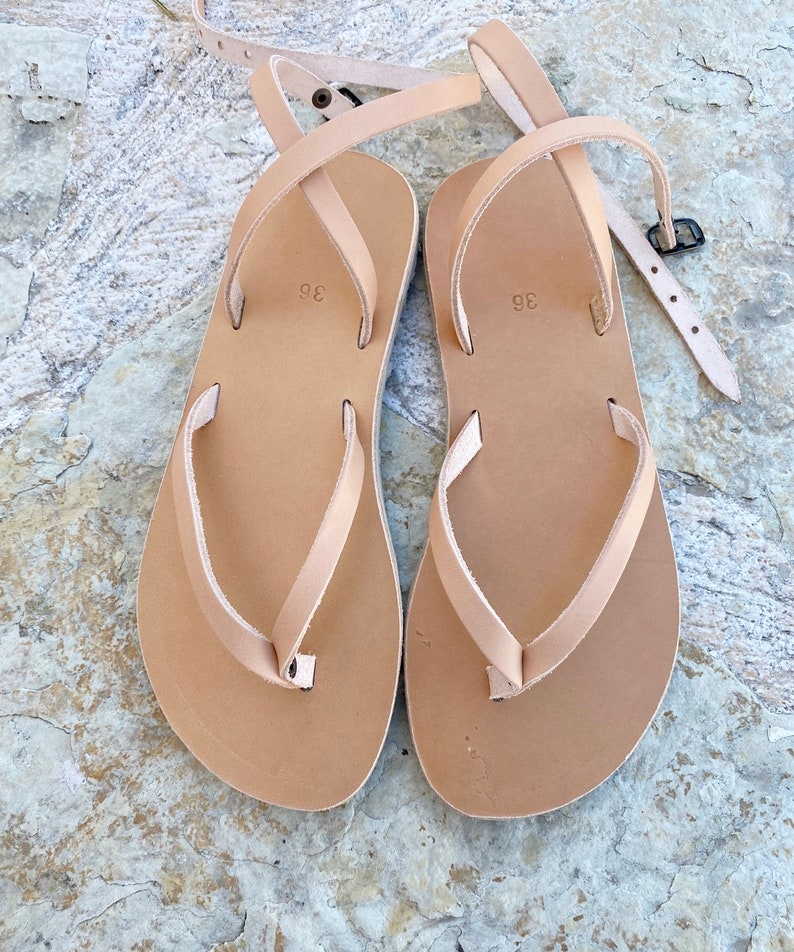 May include: A pair of tan leather sandals with a simple design. The sandals have a single strap that wraps around the ankle and a toe loop. The sandals are size 38.