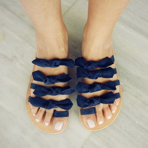 May include: A pair of sandals with multiple navy blue bows across the straps. The sandals have a brown leather sole.
