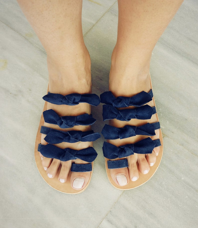 May include: A pair of sandals with multiple navy blue bows across the straps. The sandals have a brown leather sole.