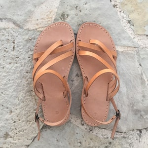 Op de afbeelding: Een paar beige leren sandalen met meerdere dunne bandjes over de wreef, een teenlus en een verstelbare enkelband met een kleine metalen gesp. Het voetbed is voorzien van het cijfer 9, wat de maat van deze platte sandalen aangeeft.