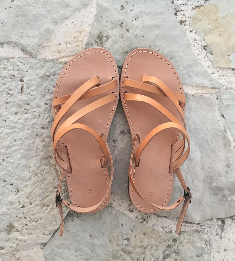 Op de afbeelding: Een paar beige leren sandalen met meerdere dunne bandjes over de wreef, een teenlus en een verstelbare enkelband met een kleine metalen gesp. Het voetbed is voorzien van het cijfer 9, wat de maat van deze platte sandalen aangeeft.