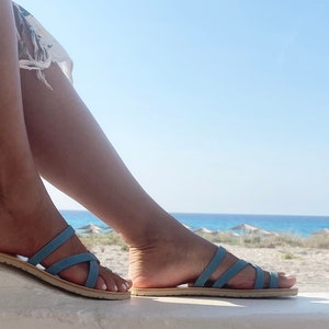 "Profile view of a woman wearing leather barefoot sandals standing by the sea, showing the zero-drop sole