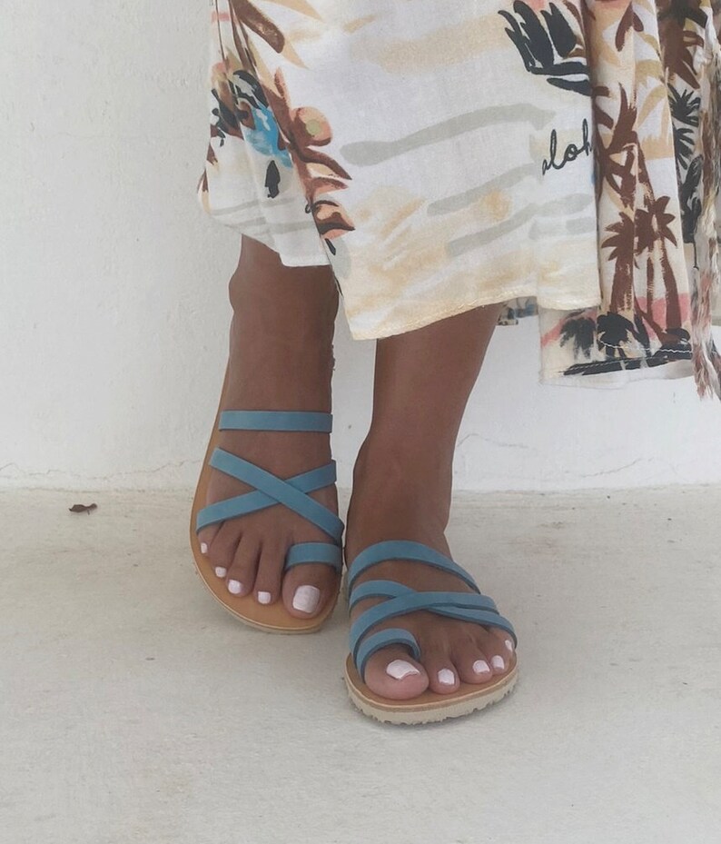A pair of blue leather sandals with criss-cross straps. The sandals have a thong style toe and a flat sole.