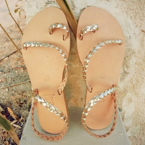 K&ouml;nnte beinhalten: Ein Paar goldene Ledersandalen mit geflochtenen Riemen. Die Sandalen sind in Griechenland hergestellt und haben eine Ledersohle.