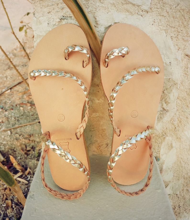 K&ouml;nnte beinhalten: Ein Paar goldene Ledersandalen mit geflochtenen Riemen. Die Sandalen sind in Griechenland hergestellt und haben eine Ledersohle.