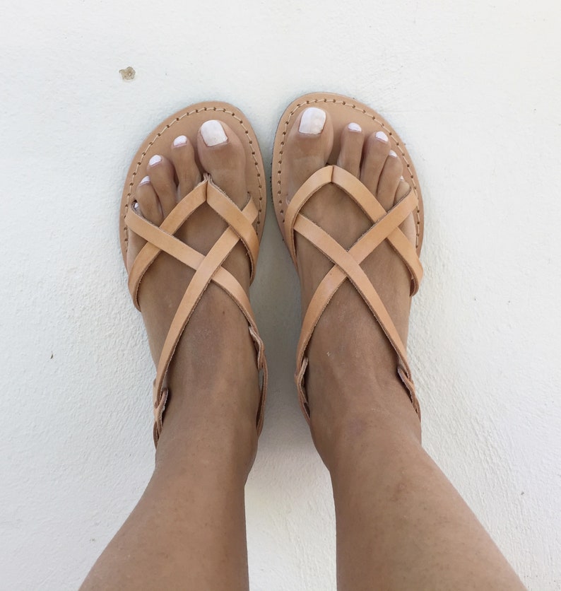 May include: A pair of tan leather sandals with criss-cross straps. The sandals have a simple design and are perfect for summer.