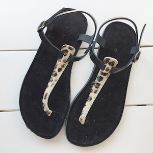 A pair of black leather sandals with a leopard print strap. The sandals have a simple design and are perfect for summer.