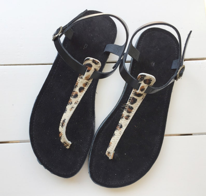 A pair of black leather sandals with a leopard print strap. The sandals have a simple design and are perfect for summer.