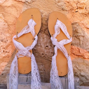May include: A pair of tan leather sandals with white lace ties. The sandals have a simple design and are tied up the legs with white lace.