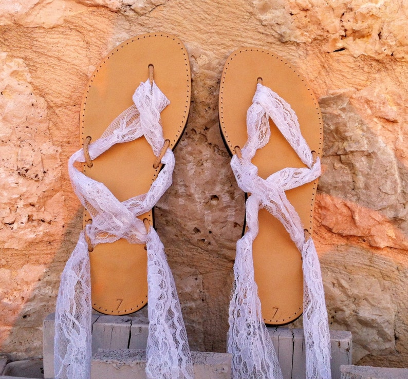 May include: A pair of tan leather sandals with white lace ties. The sandals have a simple design and are tied up the legs with white lace.