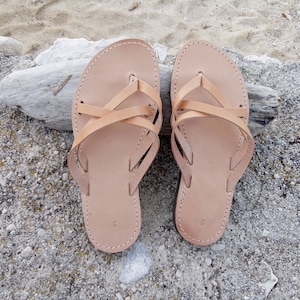 A pair of tan leather sandals with criss-cross straps. The sandals have a simple design and are perfect for summer.