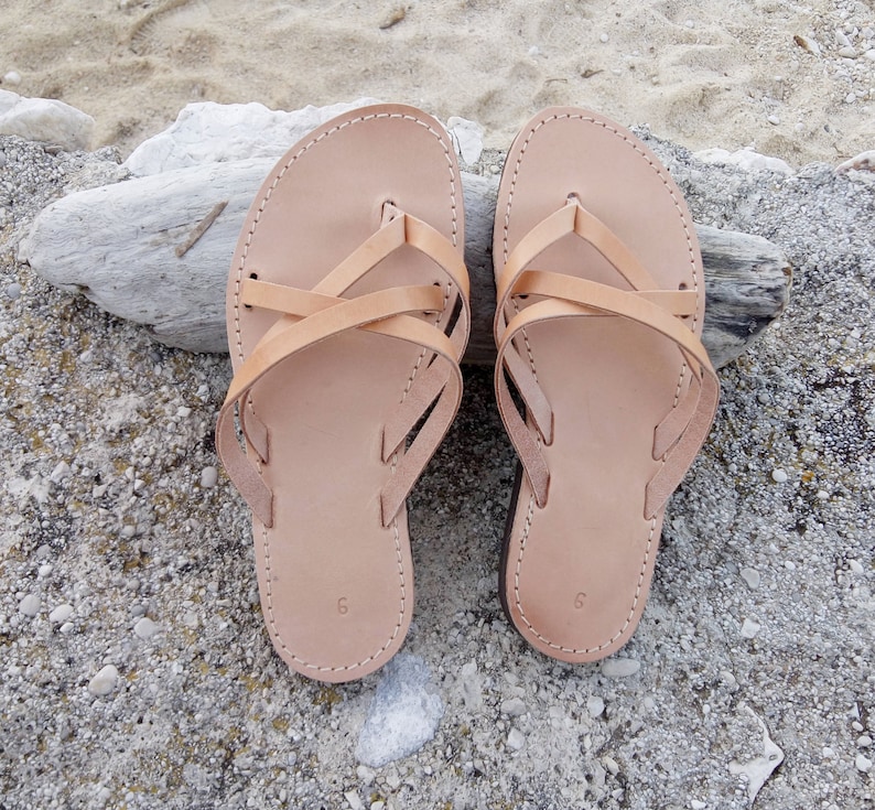 A pair of tan leather sandals with criss-cross straps. The sandals have a simple design and are perfect for summer.