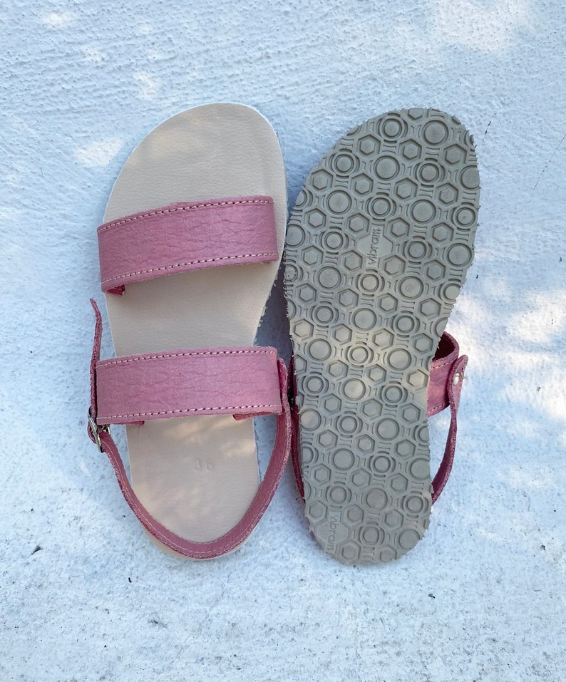 May include: A pair of sandals featuring dusty rose textured leather straps and a beige footbed with the number 36 embossed. One sandal shows the top side, while the other displays the grey rubber Vibram outsole with a hexagonal tread pattern.