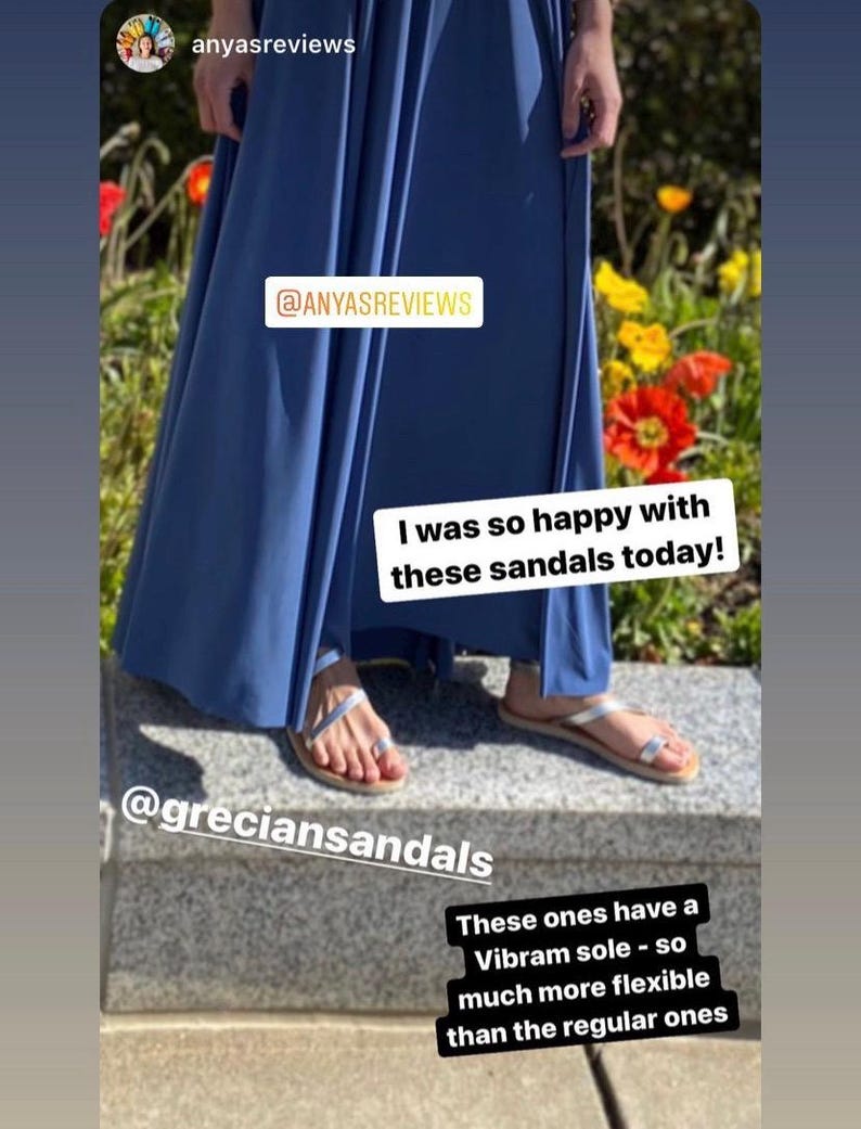 May include: Silver metallic sandals with thin straps and a toe loop, featuring a flexible Vibram sole. The sandals are worn with a long blue skirt. Text overlays include @ANYASREVIEWS, @greciansandals, I was so happy with these sandals today!, and These ones have a Vibram sole - so much more flexible than the regular ones.
