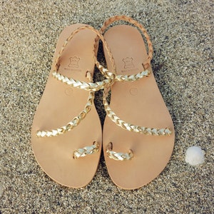 K&ouml;nnte beinhalten: Ein Paar goldene Ledersandalen mit geflochtenen Riemen. Die Sandalen sind in Griechenland hergestellt und aus echtem Leder.