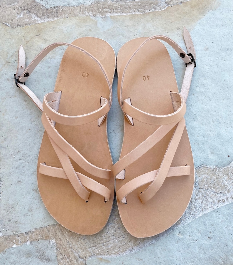 Op de afbeelding: Een paar lichtbruine leren sandalen met meerdere dunne bandjes over de voet, een teenlus en een verstelbare enkelband met een kleine metalen gesp. Het voetbed van elke sandaal is voorzien van het ingedrukte cijfer 40 voor de maat.