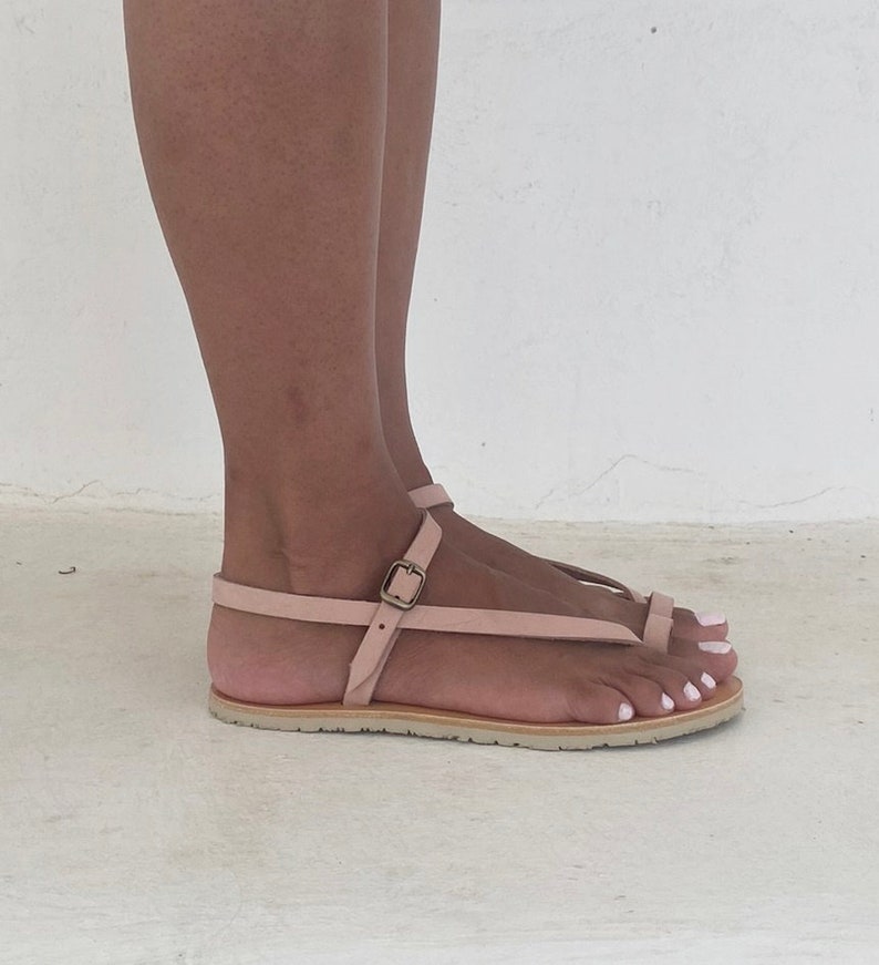 Peut inclure: Une paire de sandales en cuir rose clair avec une fermeture &agrave; boucle et une bride de style thong. Les sandales ont une semelle plate et sont faites d'un cuir souple et doux.
