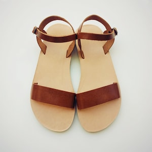 May include: A pair of brown leather sandals with ankle straps. The sandals have a simple design and are made of a soft, supple leather.