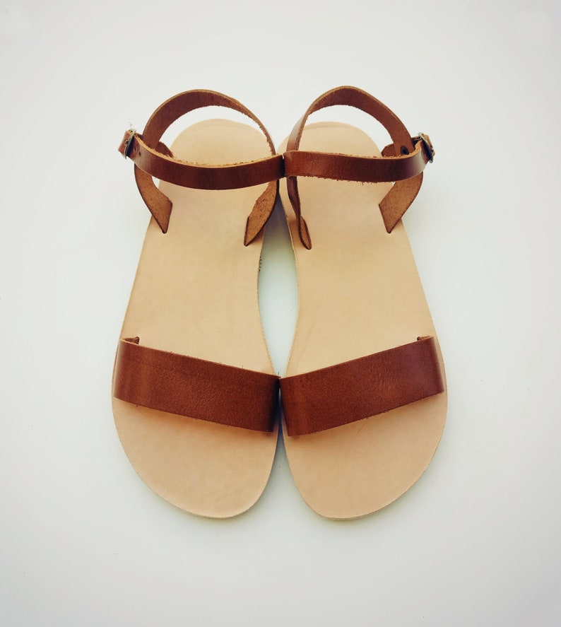May include: A pair of brown leather sandals with ankle straps. The sandals have a simple design and are made of a soft, supple leather.